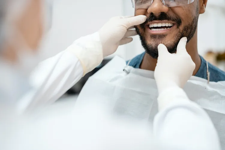Dentist examining a smiling male patient's teeth in the dental chair